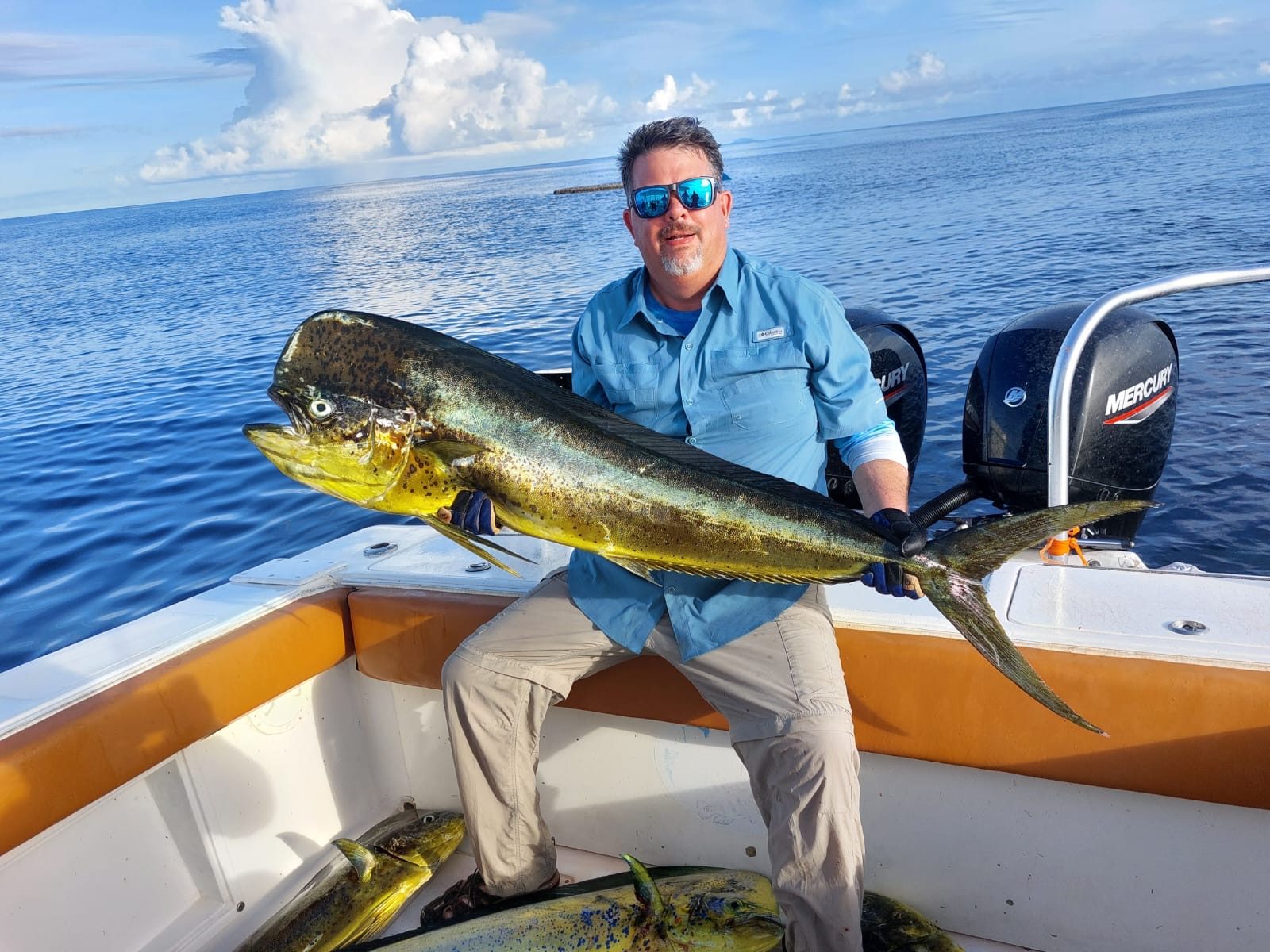 A man sitting on a boat holding a bright mahi-mahi