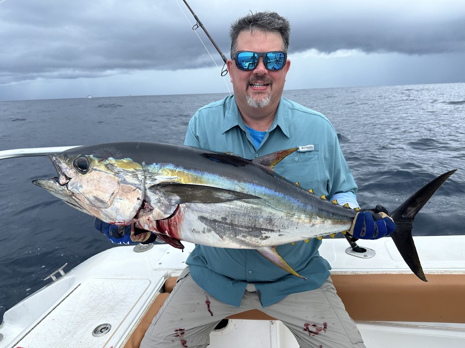 A man holding a large yellowfin tuna on a fishing boat